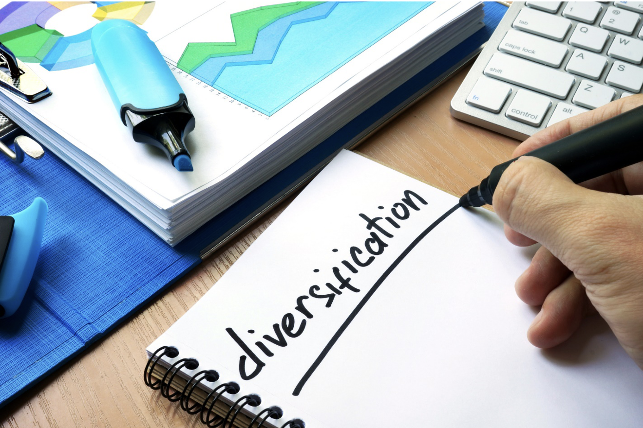 a person writing the word diversification on a piece of paper next to a keyboard.