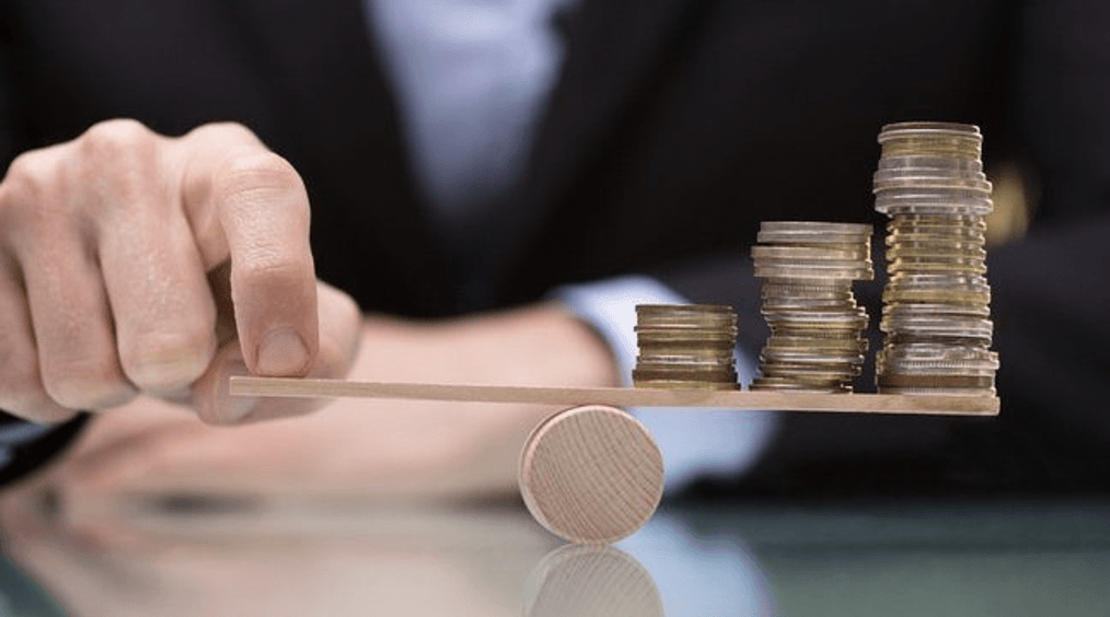 Coins on the end of a wood platform with a businessman balancing the uneven weight with his hand