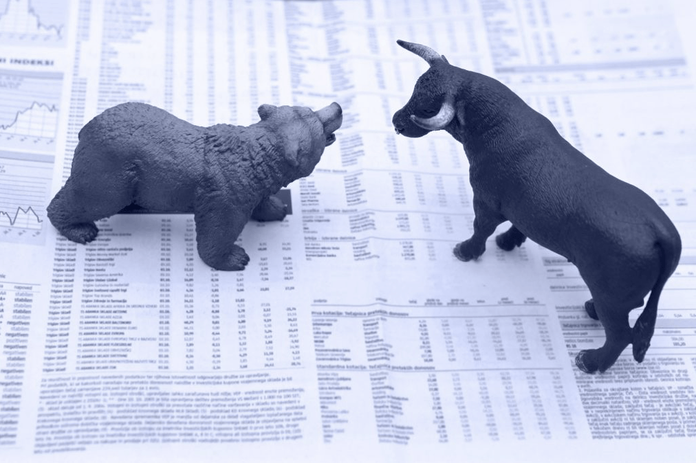 A toy bull and bear sitting on top of a finance paper