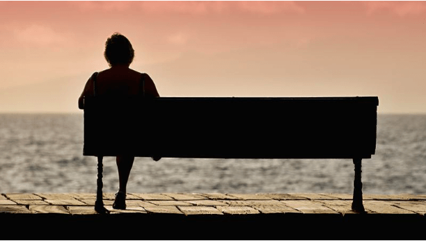 A retired woman sitting on a bench near the ocean