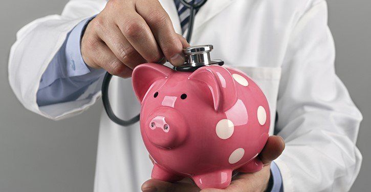 a doctor holding a pink piggy bank with a stethoscope.