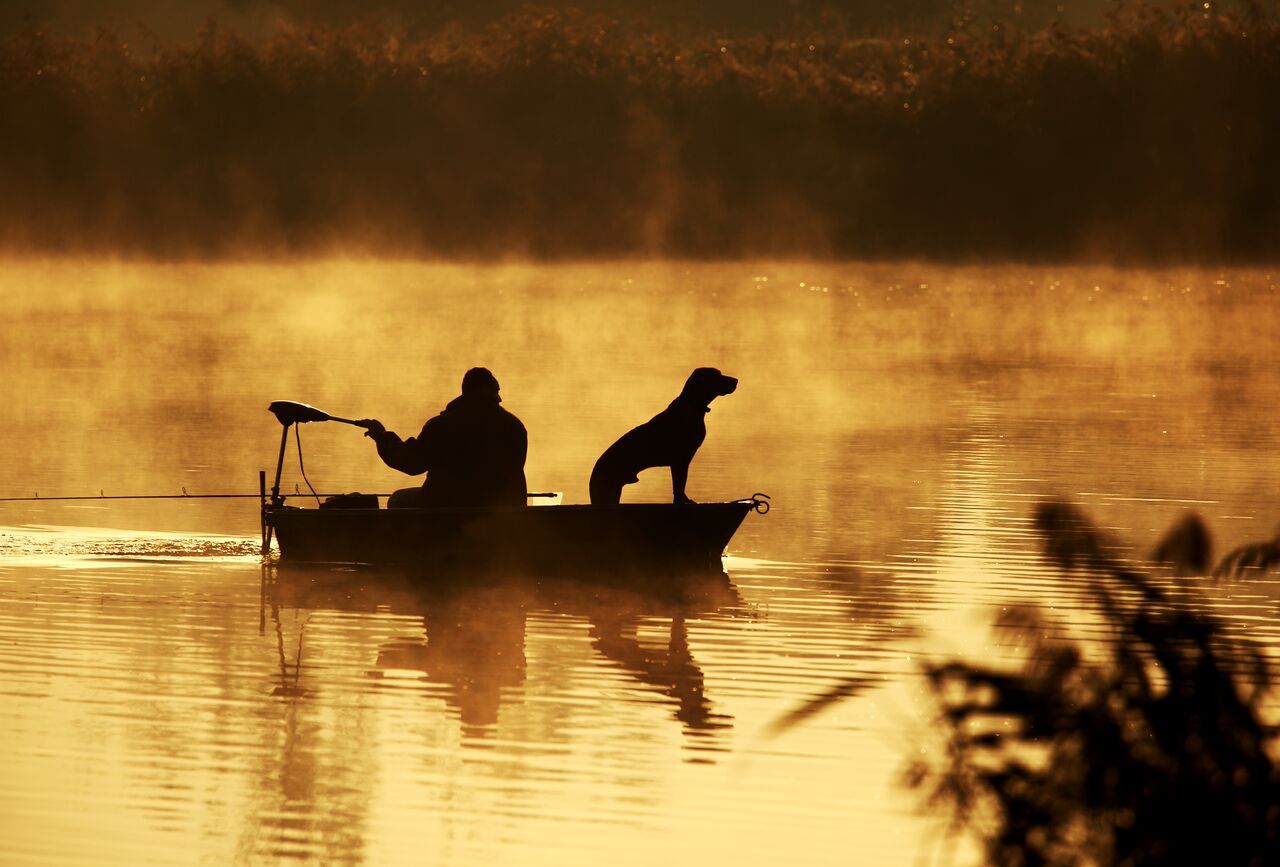 Man living his ideal life fishing with his dog on his Canoe during sunrise