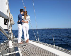 A man and woman standing on the deck of a sailboat living their ideal life.