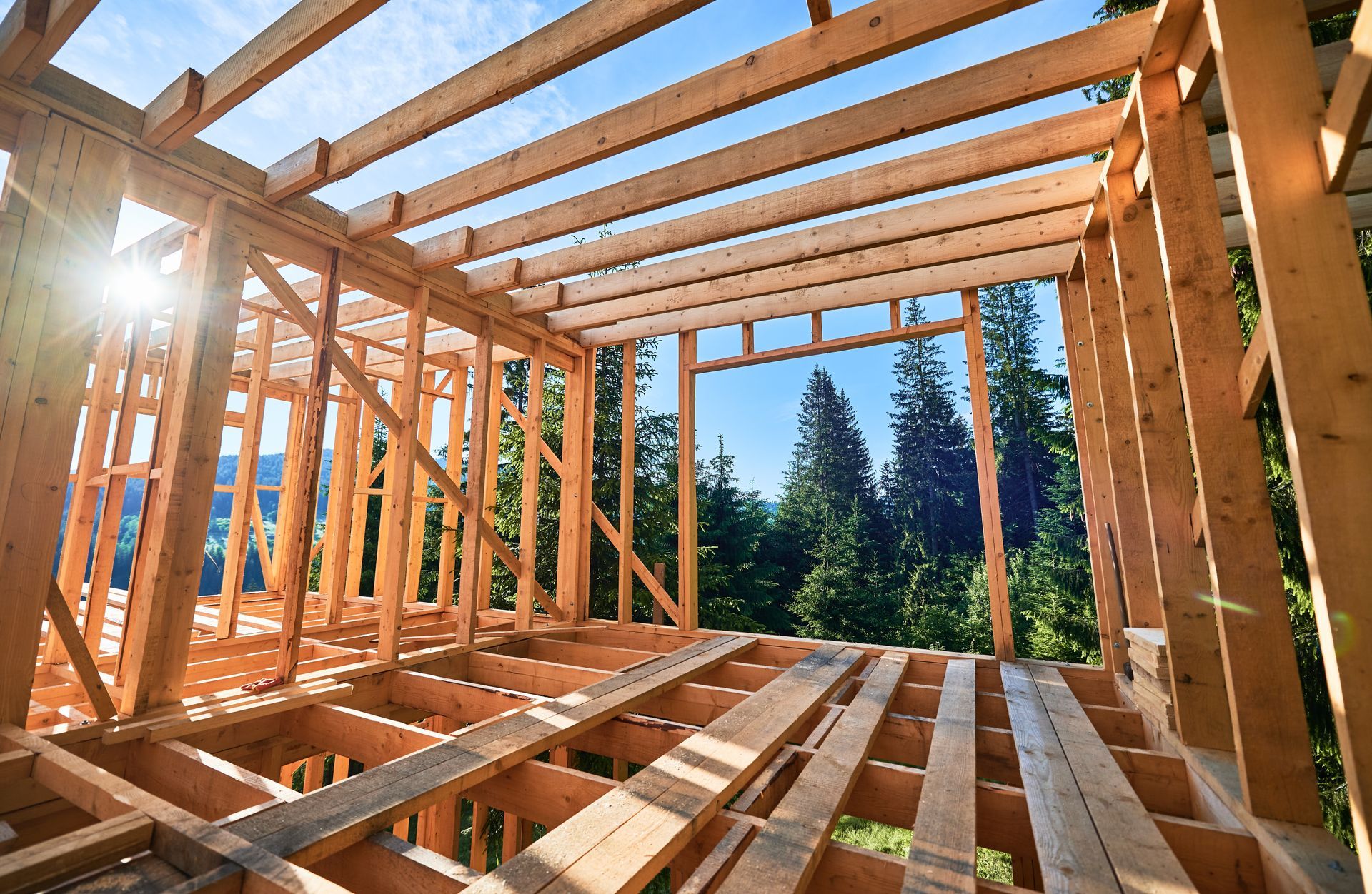 A house is being built out of wood and the sun is shining through the trees.