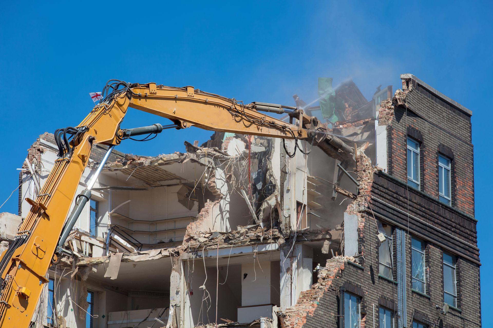 A large yellow excavator is demolishing a large brick building.