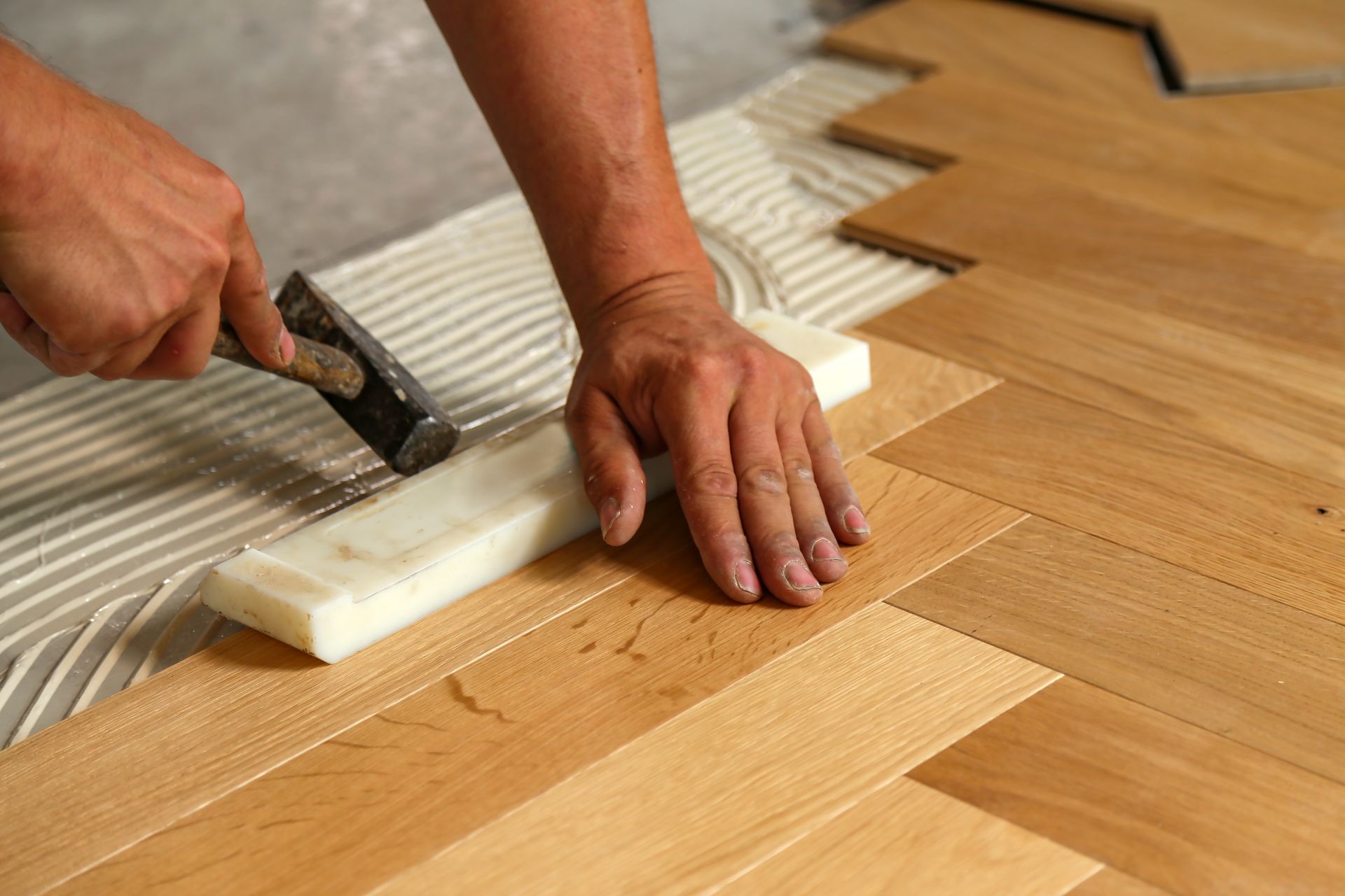 A person is using a hammer to apply adhesive to a wooden floor.