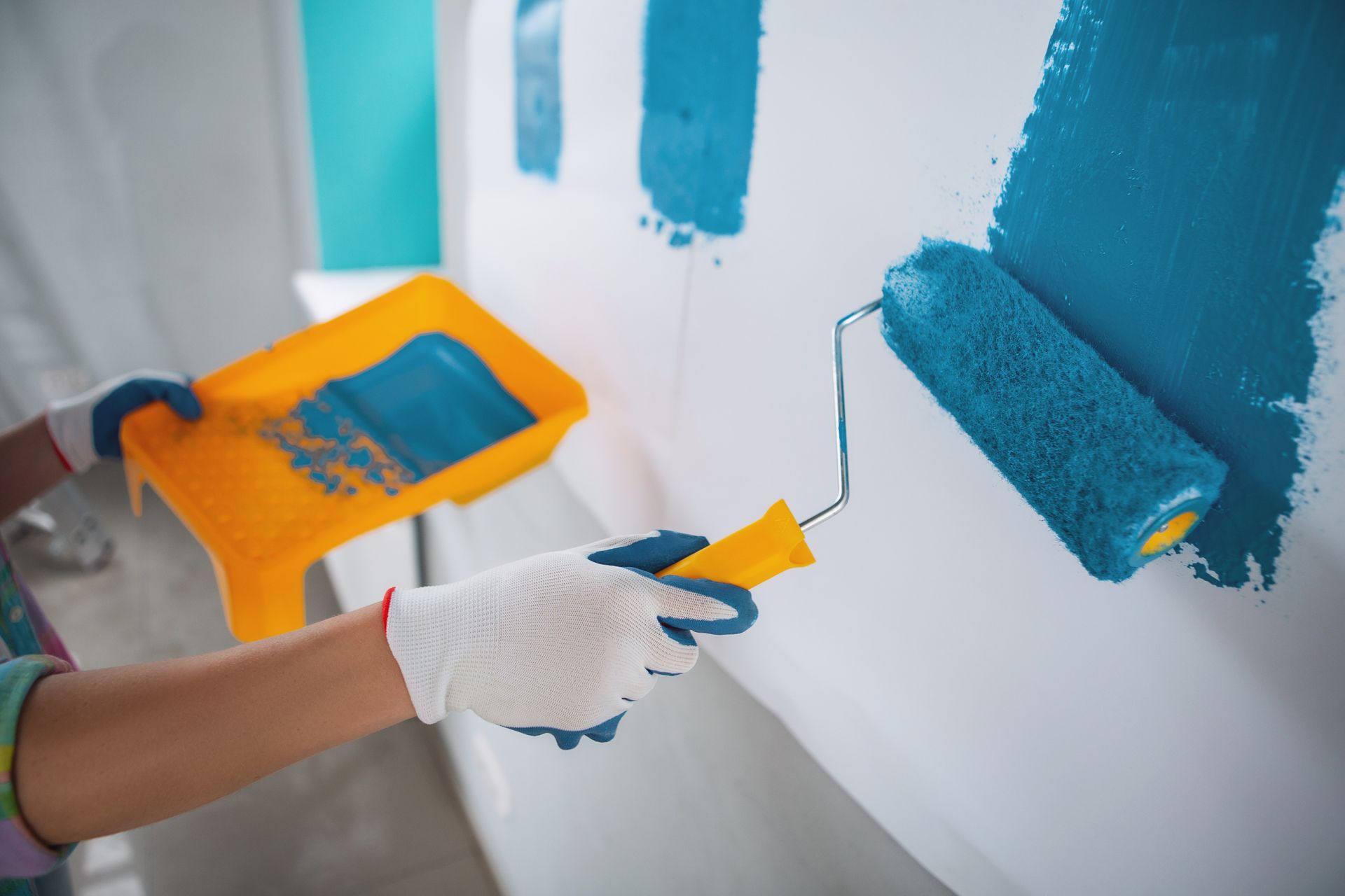 A person is painting a wall with a blue paint roller.