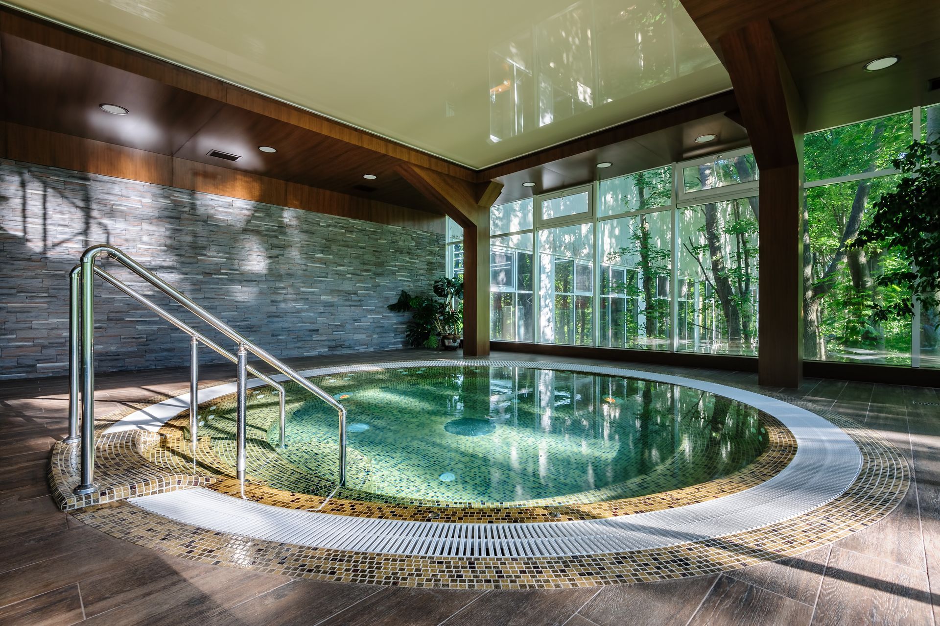 Spa intérieur avec piscine ronde et mains courantes, entouré de fenêtres et de murs en pierre.