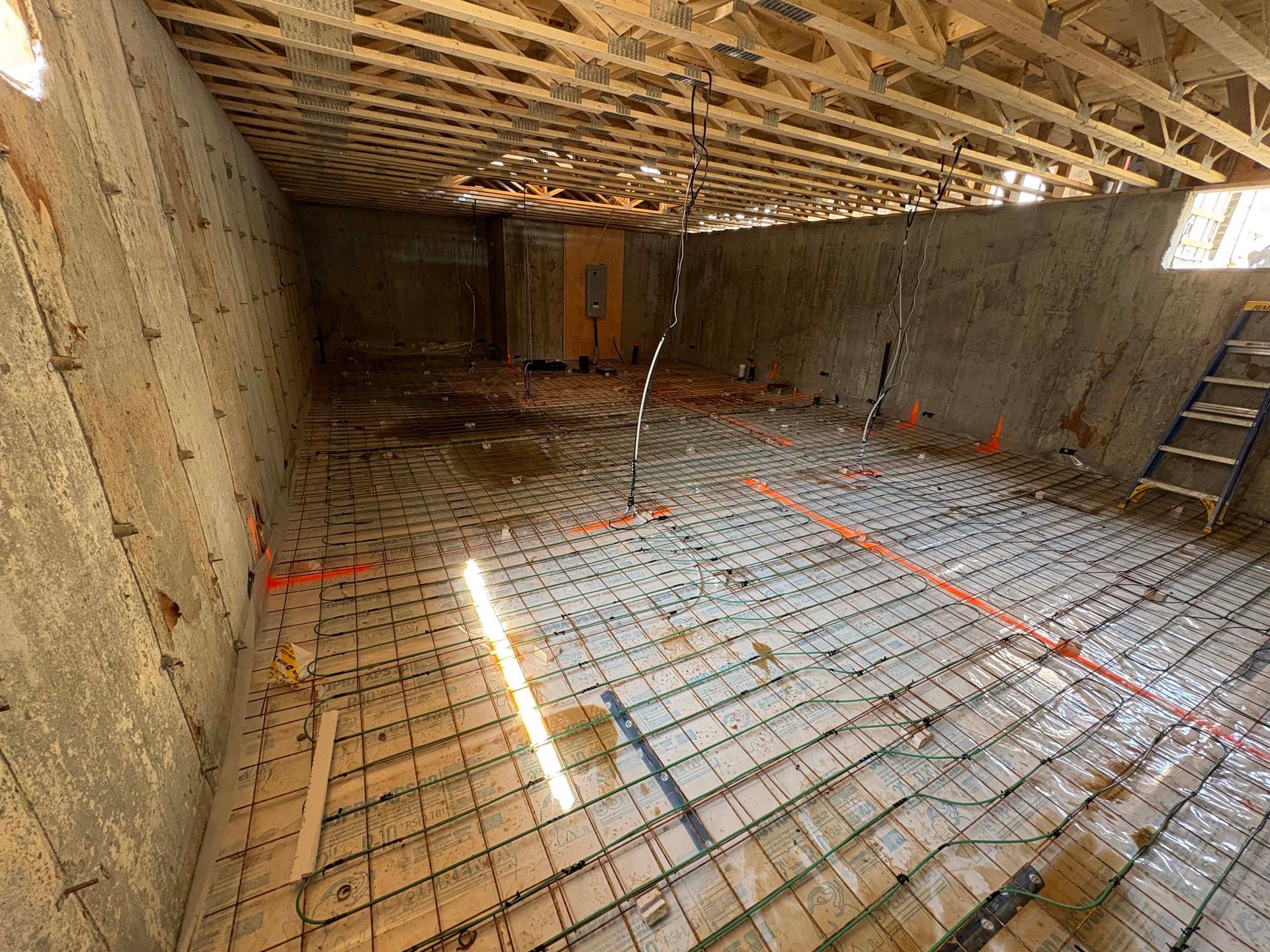 Sous-sol en construction, avec plancher en béton, câblage apparent, poutres en bois et échelle.