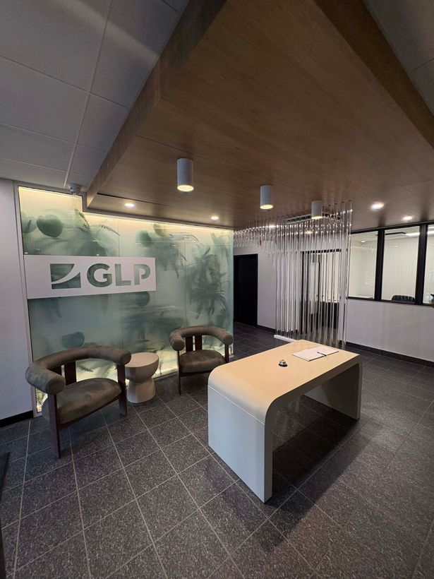 Espace de réception du bureau GLP avec logo sur un mur végétal, mobilier moderne et plafond en bois clair.
