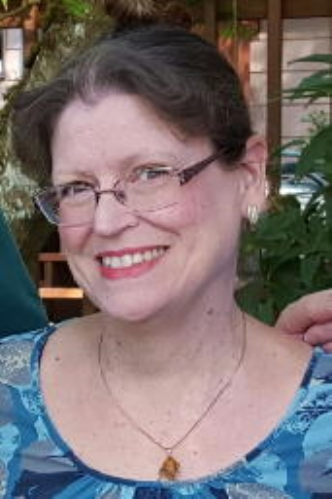 A woman wearing glasses and a necklace is smiling for the camera.
