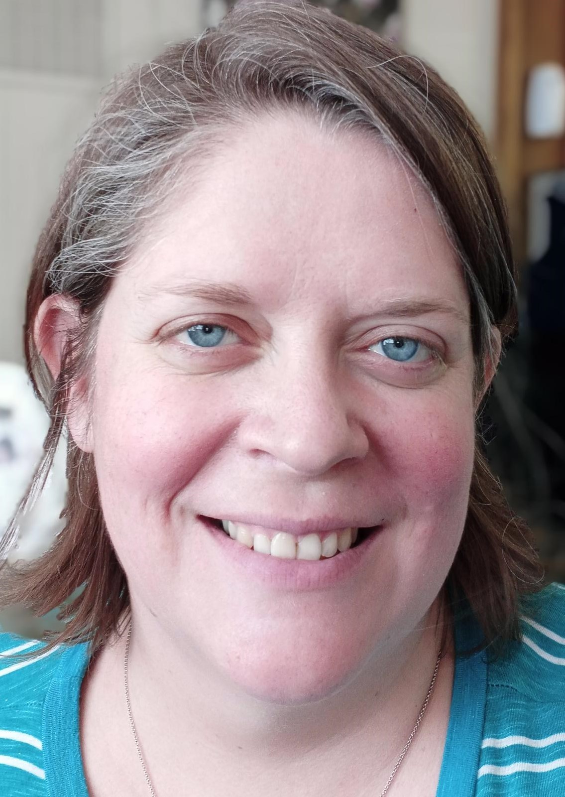 A woman with blue eyes and brown hair is smiling for the camera.
