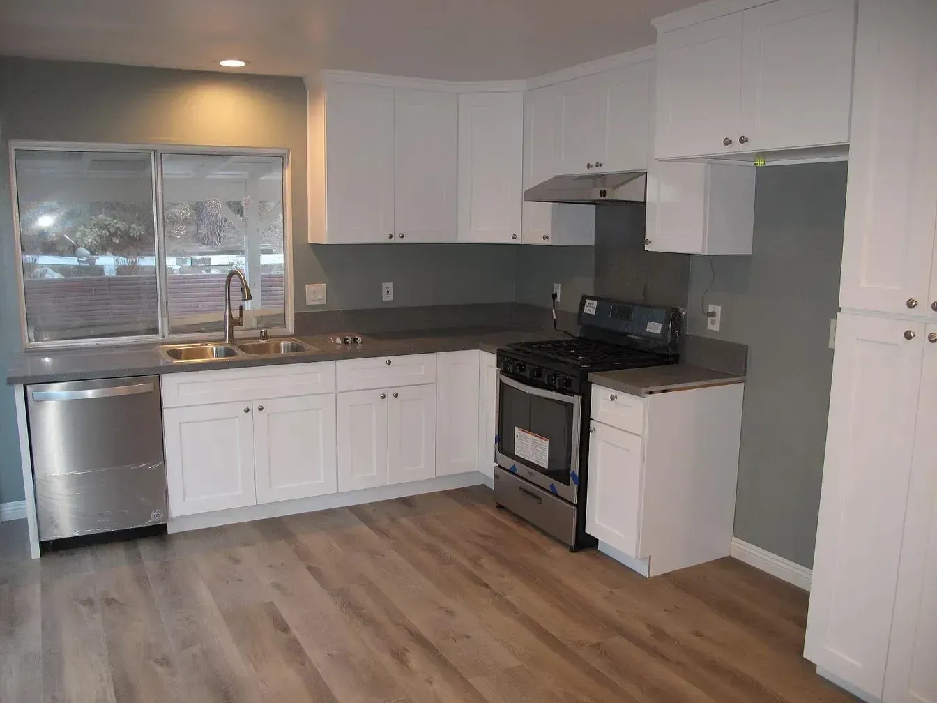 Bright kitchen with white cabinets, stainless steel appliances, and grey countertops against a grey wall.