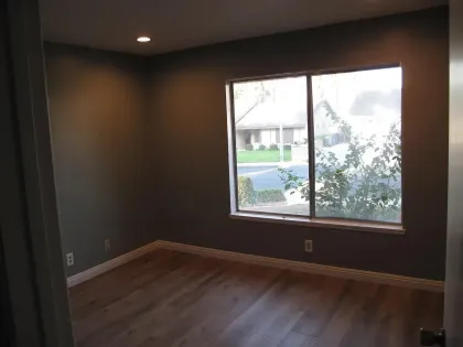 Empty room with brown walls, wood floor, and a window overlooking a residential street.