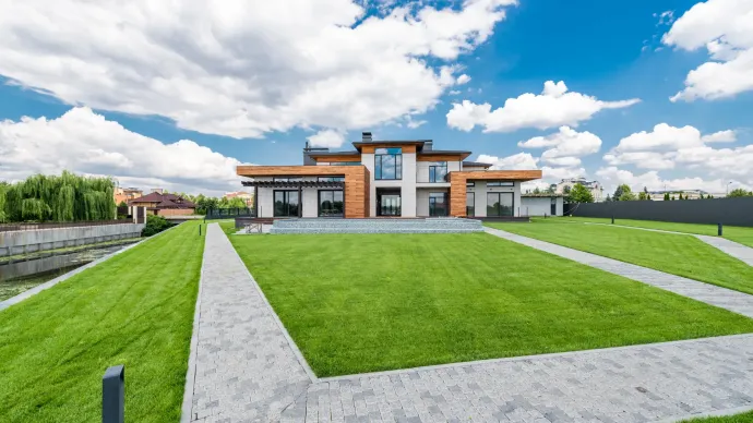 Modern house with a manicured green lawn, stone pathways, and blue sky with clouds.