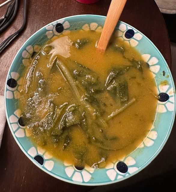 Bowl of soup with green leafy vegetables and a wooden spoon.