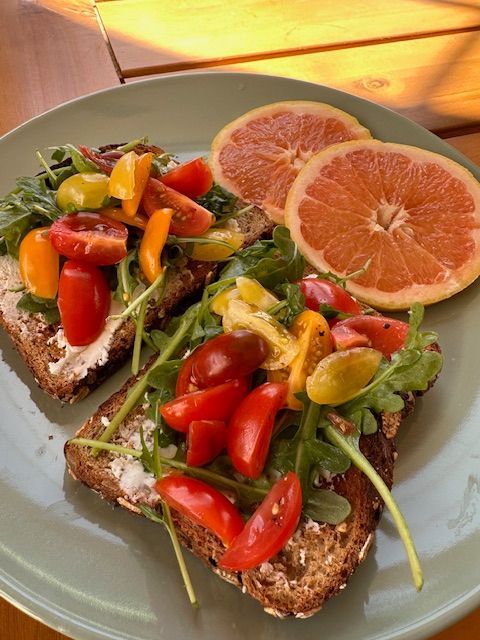 Toasted bread topped with arugula, colorful tomatoes, and grapefruit slices on a plate.