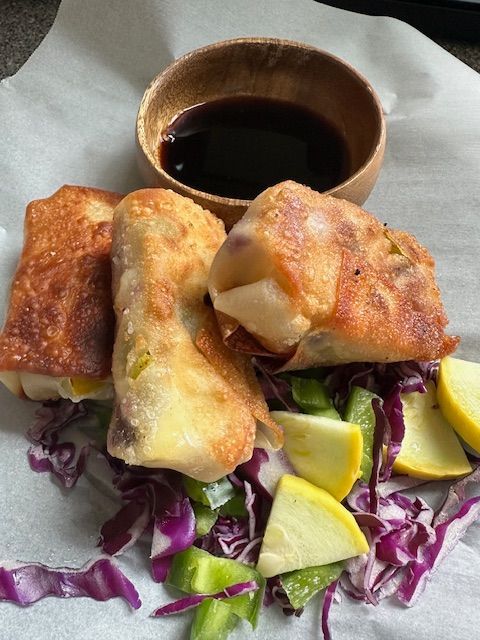 Fried spring rolls, soy sauce, and chopped vegetables on parchment paper.