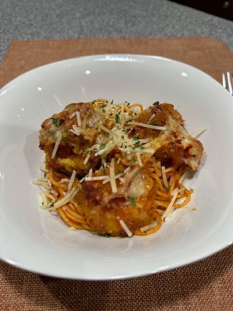 Squash parmesan served over spaghetti in a white bowl, garnished with cheese.