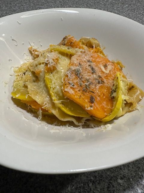 Casserole of layered yellow squash and butternut squash in a white bowl, sprinkled with cheese.