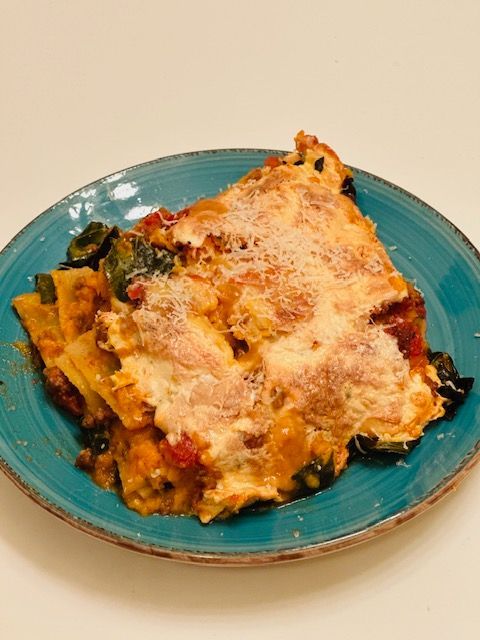 Lasagna slice on a teal plate, with cheese, sweet potato, and kale.