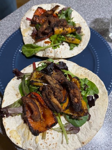 Two vegetable tacos on a blue plate, with grilled peppers and greens.