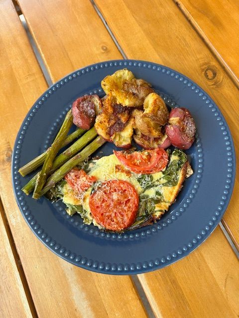 Plate of food: frittata, asparagus, roasted potatoes, and tomato slices on a blue plate.