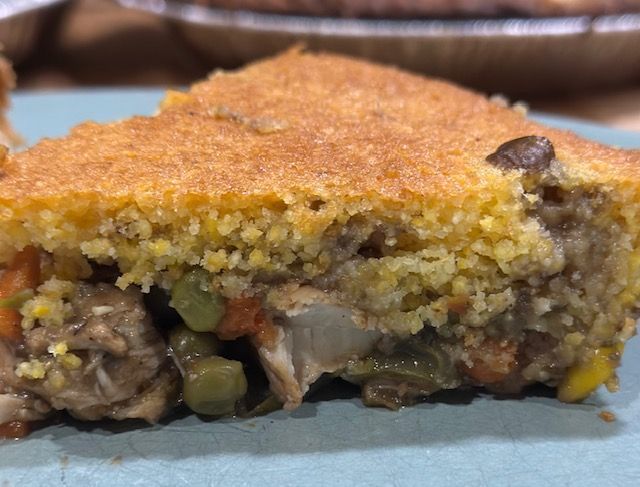 Slice of savory pie with cornbread crust, filled with vegetables and meat.