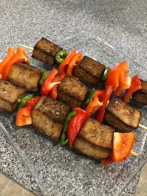 Tofu and vegetable skewers on a glass plate, with red bell pepper and green pepper.