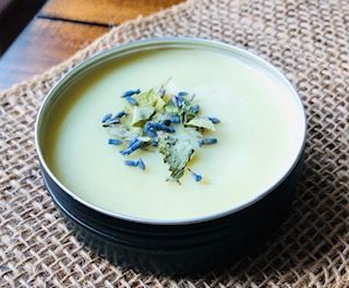 Creamy balm in a metal tin, topped with dried lavender and herbs.