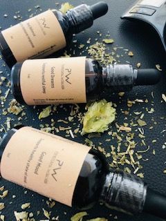 Three bottles of aromatherapy oil with plant leaves, on a black surface.