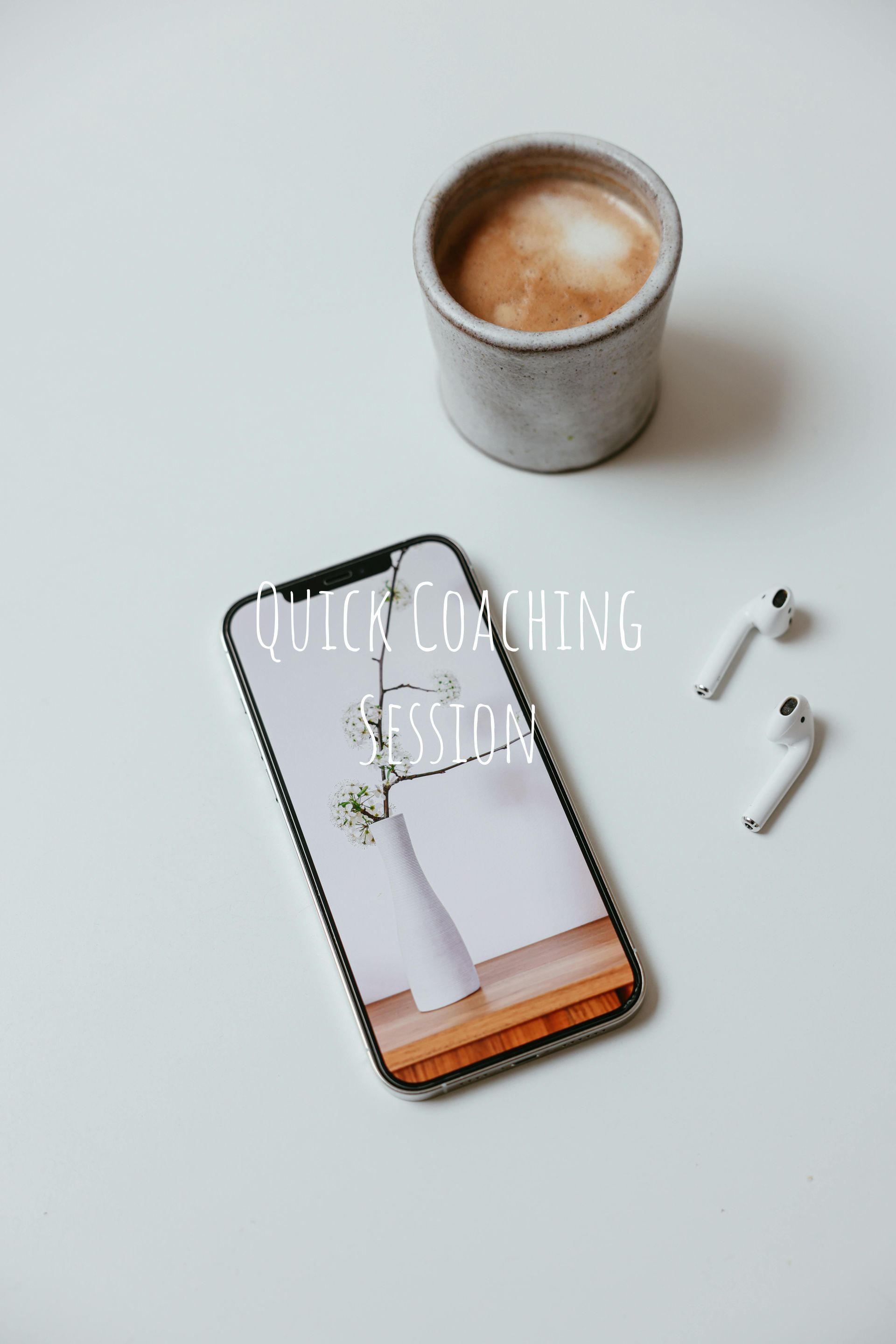 Smartphone with a vase and flower image, next to a coffee cup and earbuds on a white surface.