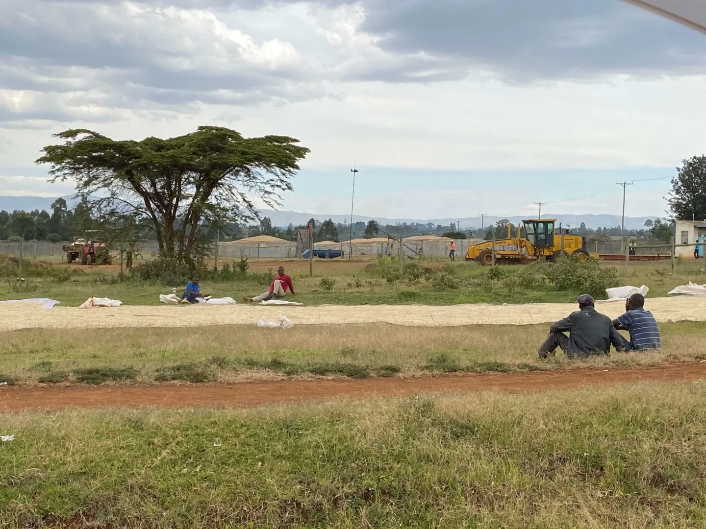 Two men are sitting in a field with tractors in the background