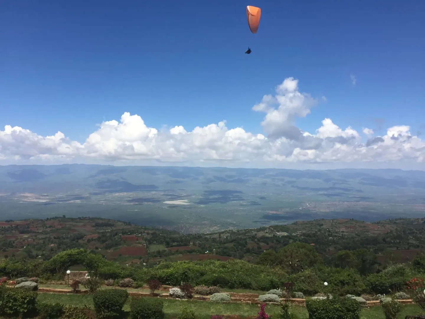 A person is parasailing over a lush green valley.