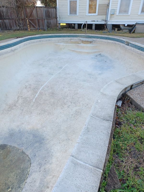 An empty, stained plaster swimming pool with a tiled border and light-colored coping, located in a backyard.