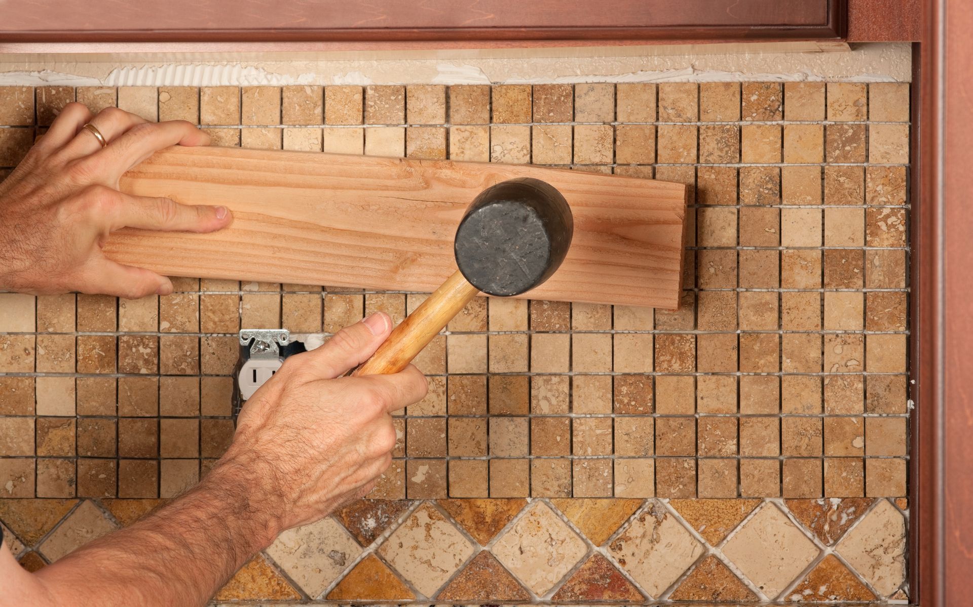 A man is hammering a piece of wood on a tiled wall.