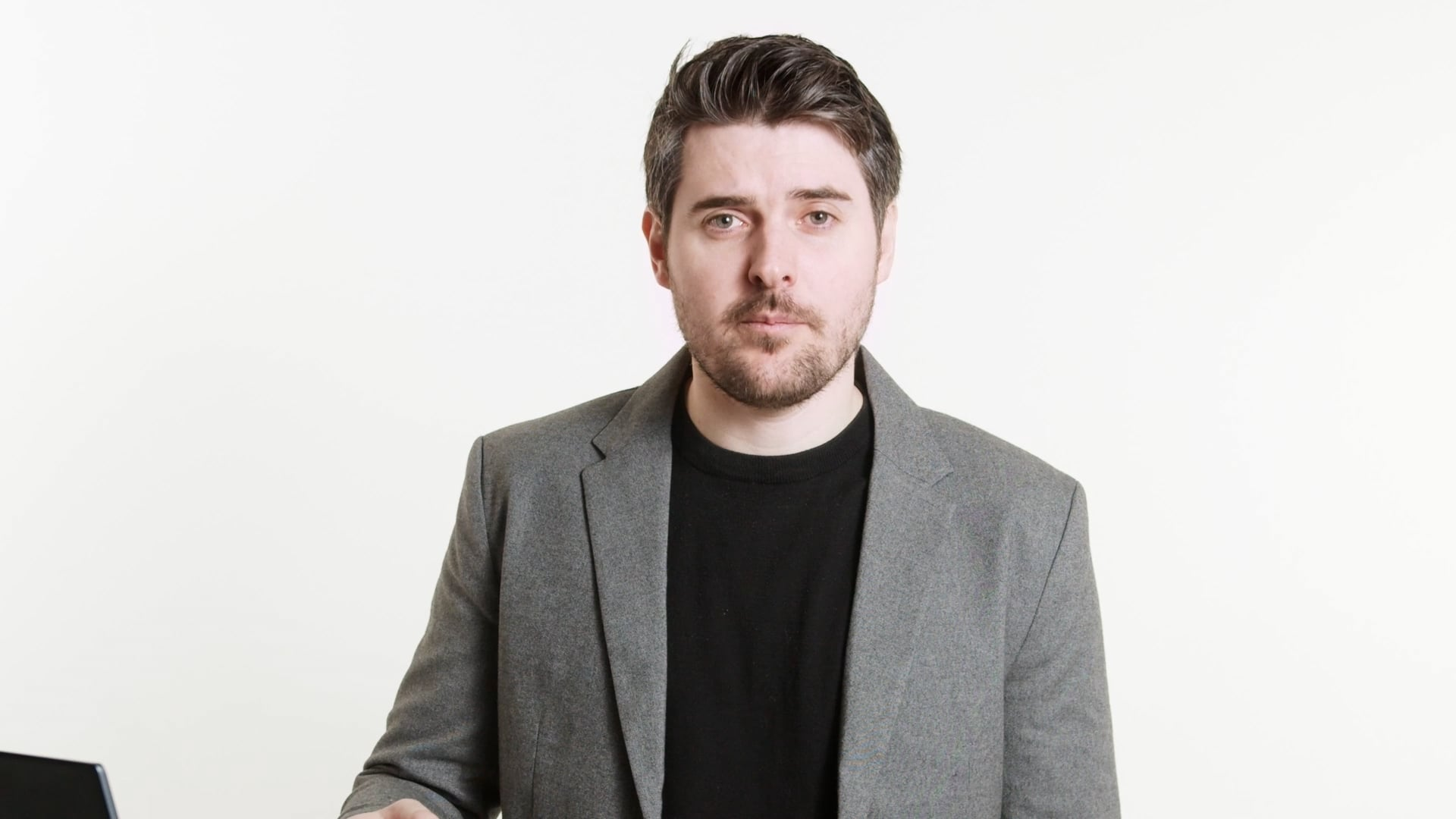 Man in a gray blazer over a black shirt standing against a white background