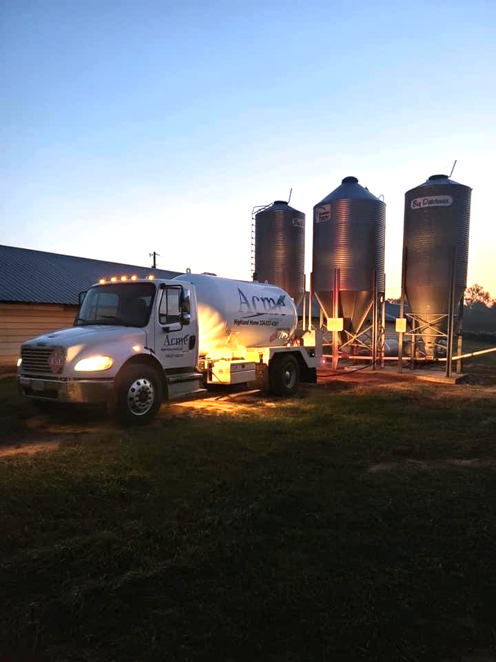 A white Acme bobtail truck is parked in front of three silos.