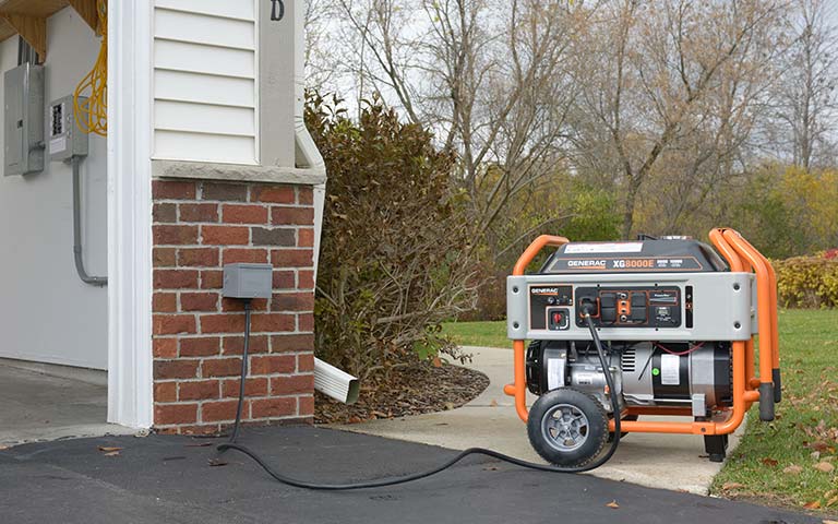 A generator is plugged into a brick wall next to a garage.