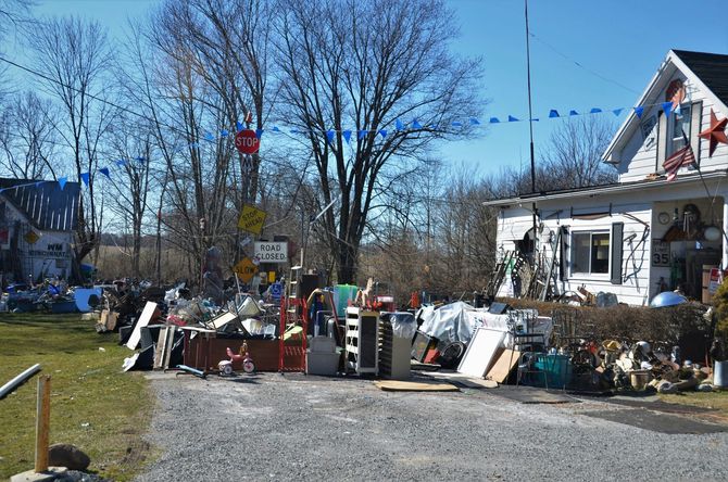 Yard sale tables and assorted items piled along a residential street under a clear blue sky