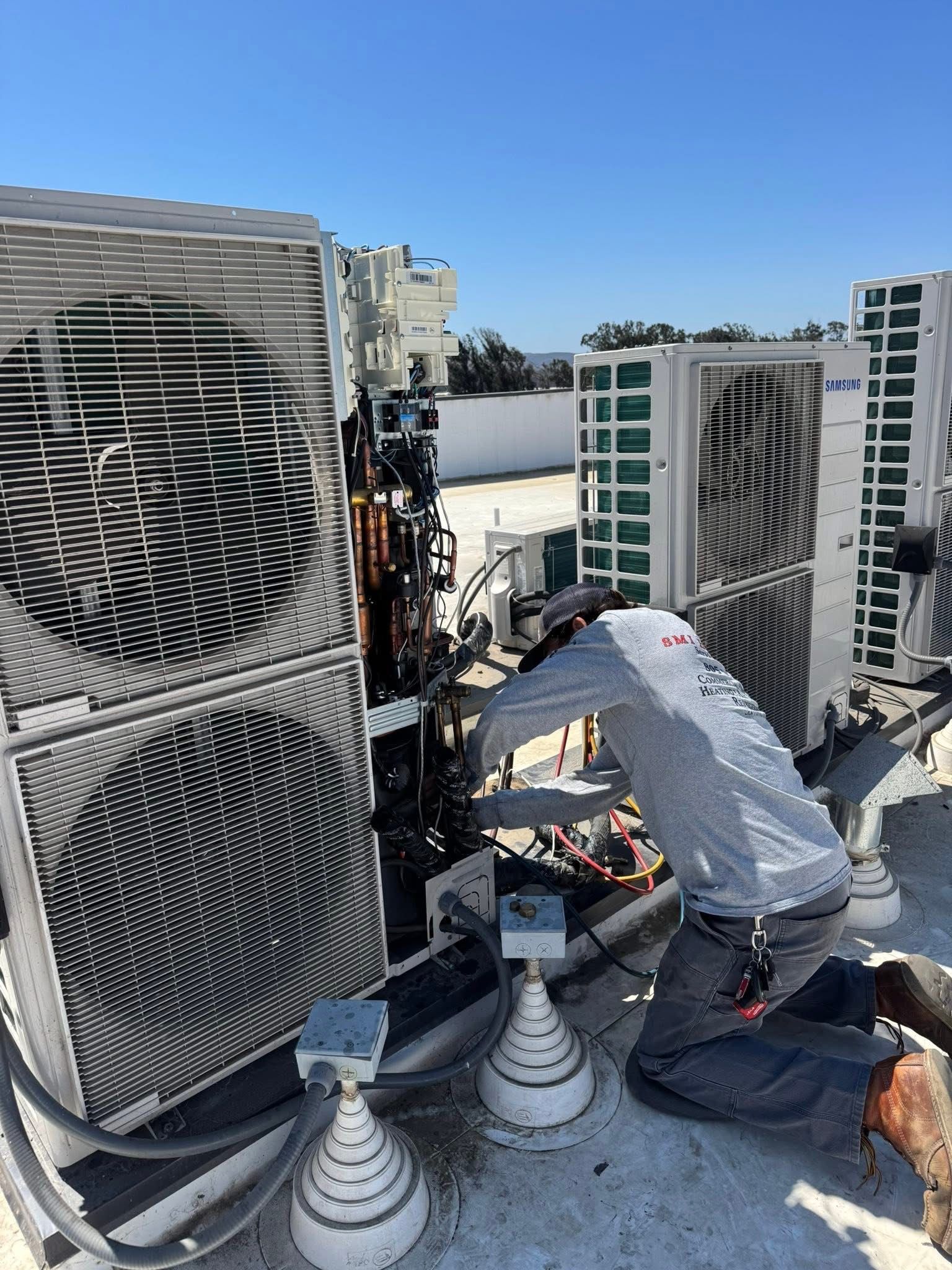 Person in orange work clothes repairing RV air conditioner on a white roof.
