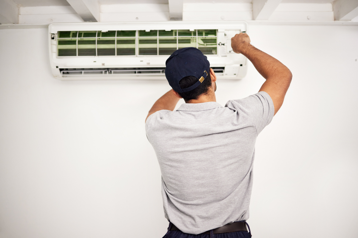 Man in cap and gloves installs air conditioner on wall.