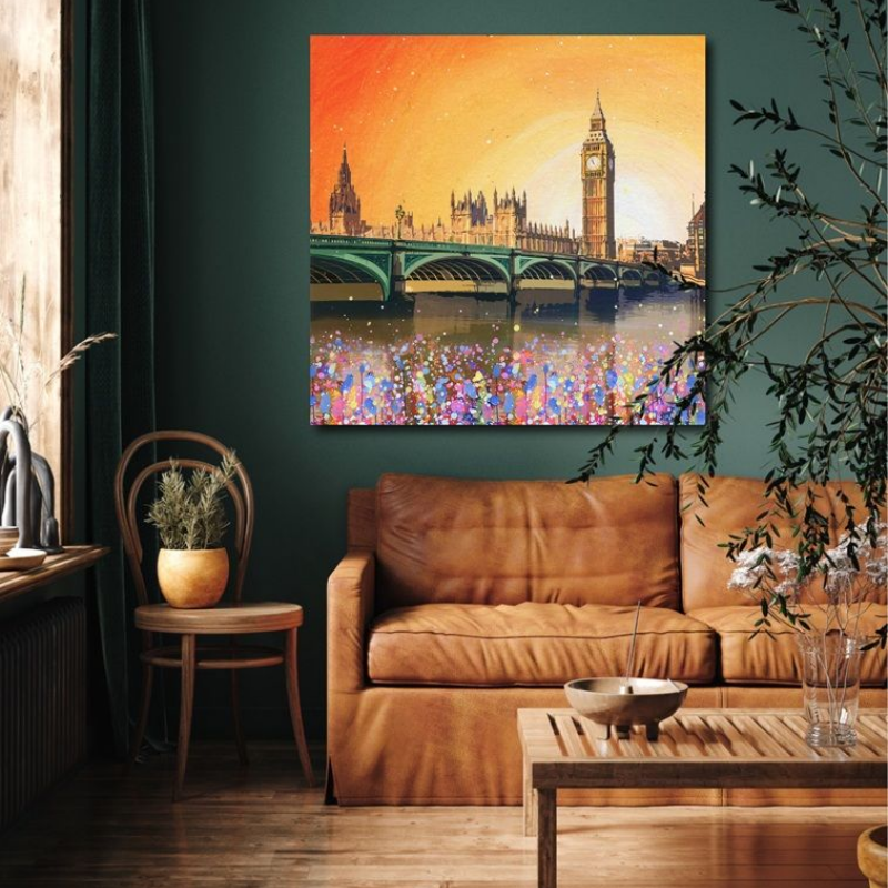 Big Ben and the Houses of Parliament at sunset, reflected in the water, over a brown leather couch in a dark room.