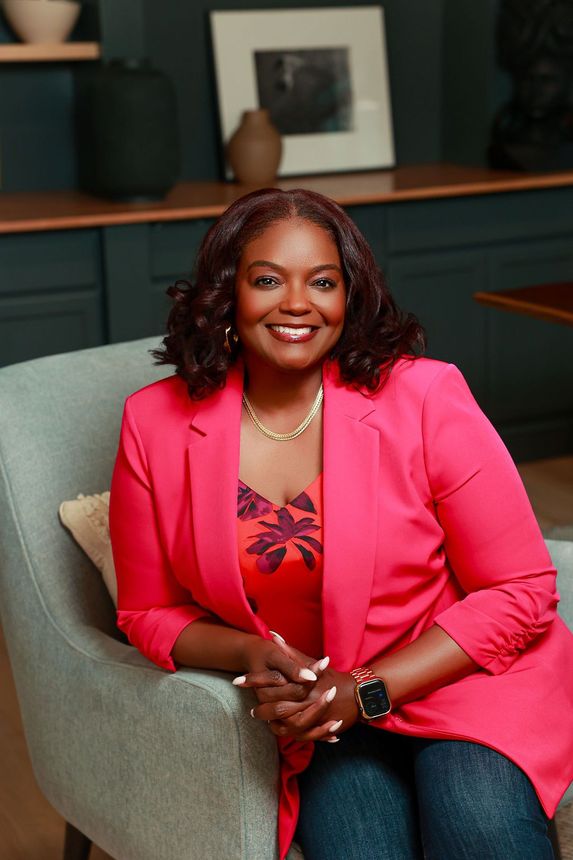A woman is sitting at a desk with a laptop and a vase of flowers.