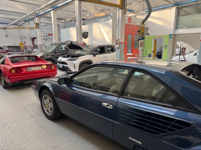 In un'officina meccanica, un meccanico in tuta da lavoro utilizza una ventosa blu per sollevare il parabrezza di un'auto.