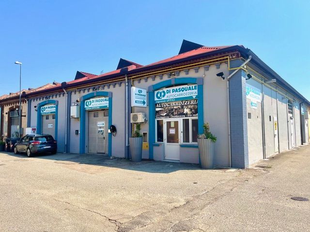 In un'officina, un veicolo con il cofano aperto è in fase di riparazione, collegato in primo piano ad apparecchiature diagnostiche o di servizio.