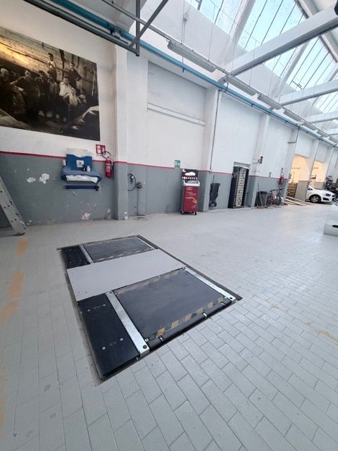 Un meccanico tiene in mano un mazzo di chiavi inglesi in un'officina meccanica, con un'auto su un ponte sollevatore sullo sfondo.