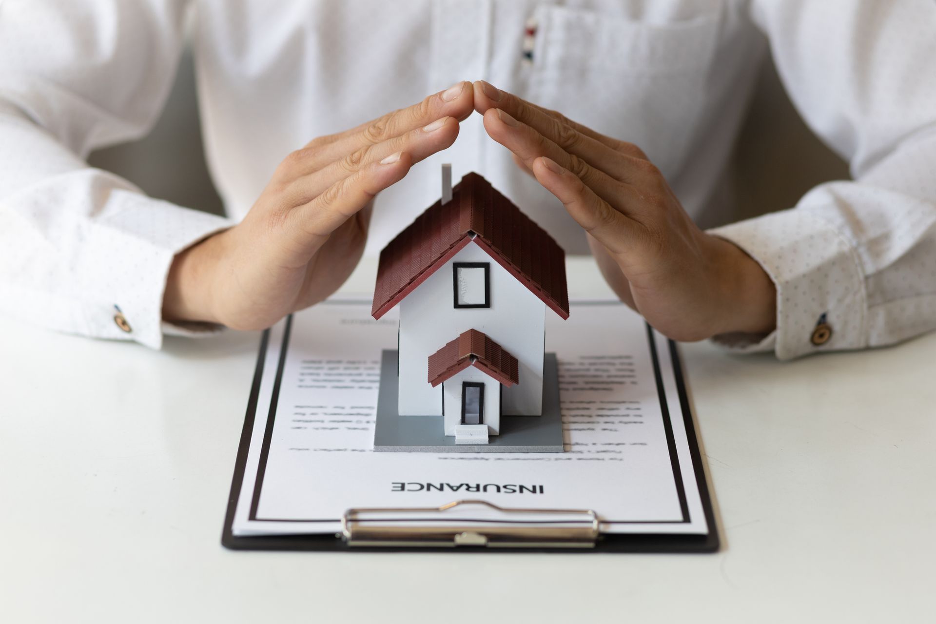 A home insurance agent forming a house with his hands with a home insurance agreement on his desk.