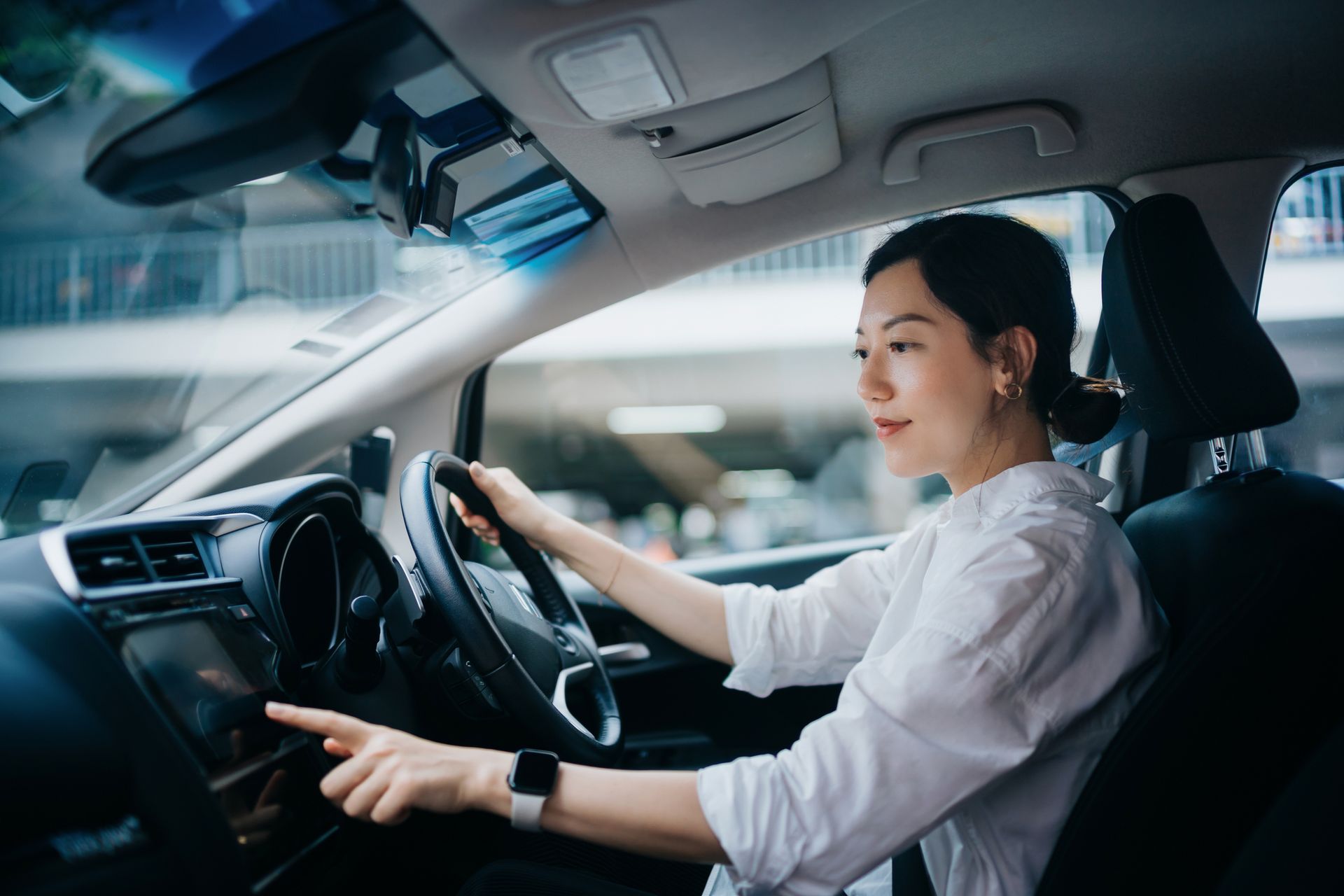 A female driver inside a car is using the touchscreen while holding the steering wheel.