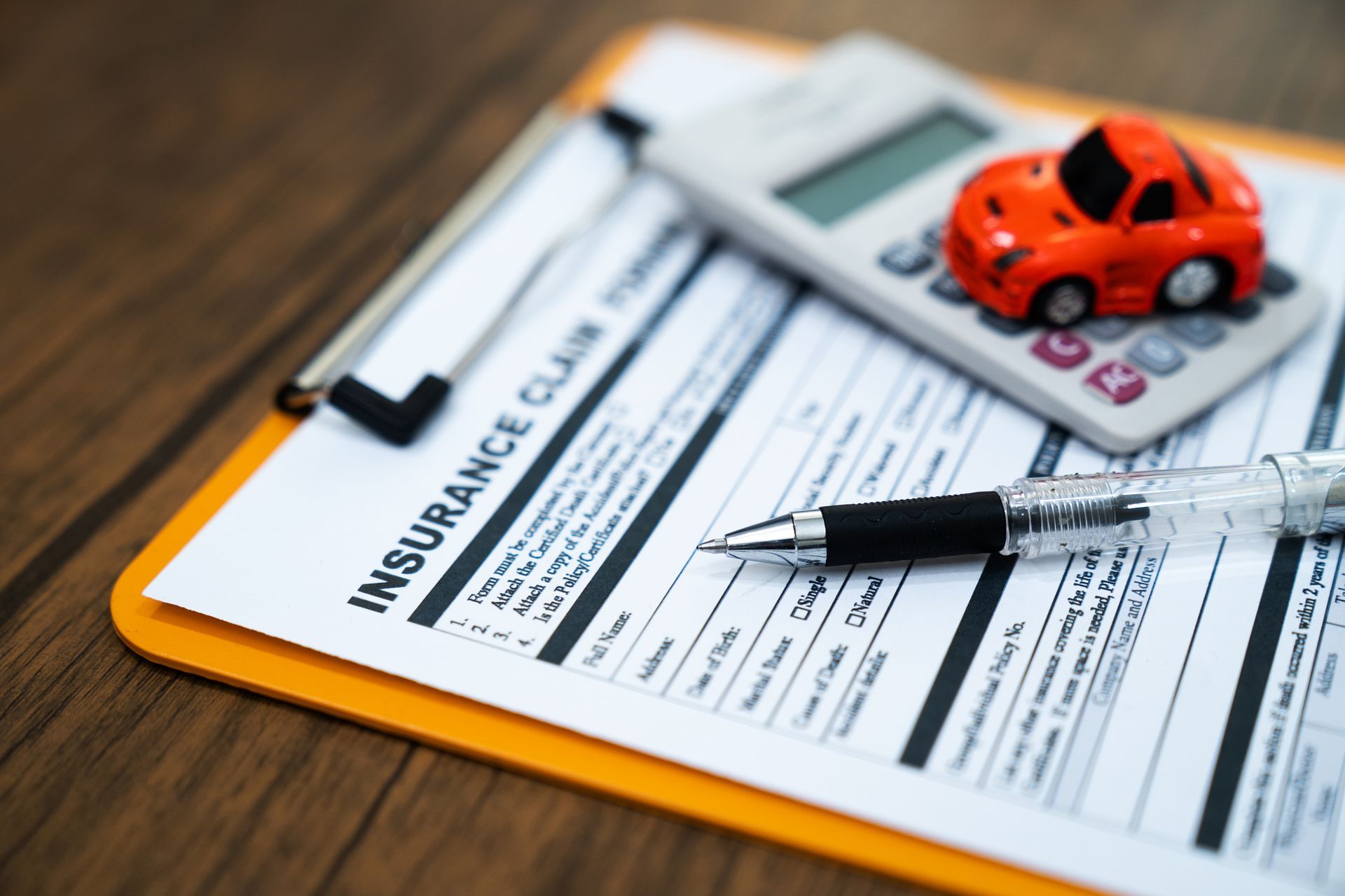 Insurance claim form with pen, calculator, and toy car on a wooden desk